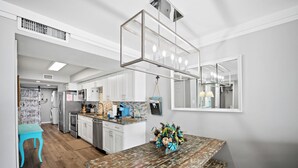 Una cocina moderna con armarios blancos, una mesa de comedor de madera y una lámpara colgante.