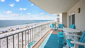 Un balcón con vistas a la playa, una piscina y mobiliario exterior.