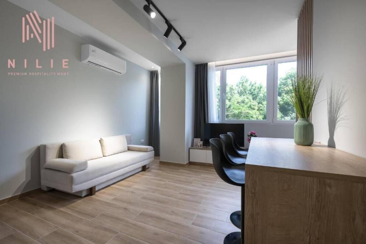 Una habitación de hotel moderna con sofá, un escritorio de madera y un ventanal con vistas a zonas verdes.