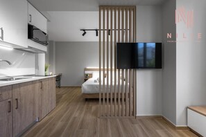 A modern hotel room with a kitchenette, a bed, a TV, and a sliding door. - Ultima Suites Nilie Hospitality MGMT (Thessaloniki)