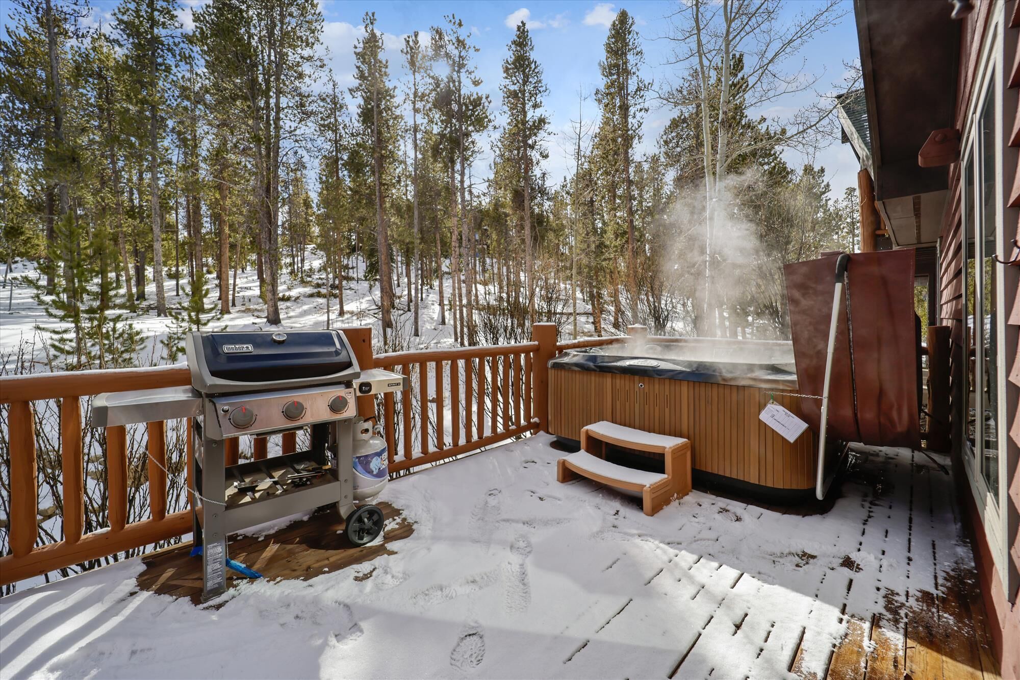 A wooden deck with a barbecue grill, a hot tub, and a wooden bench.