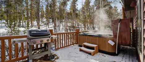 A wooden deck with a barbecue grill, a hot tub, and a wooden bench.