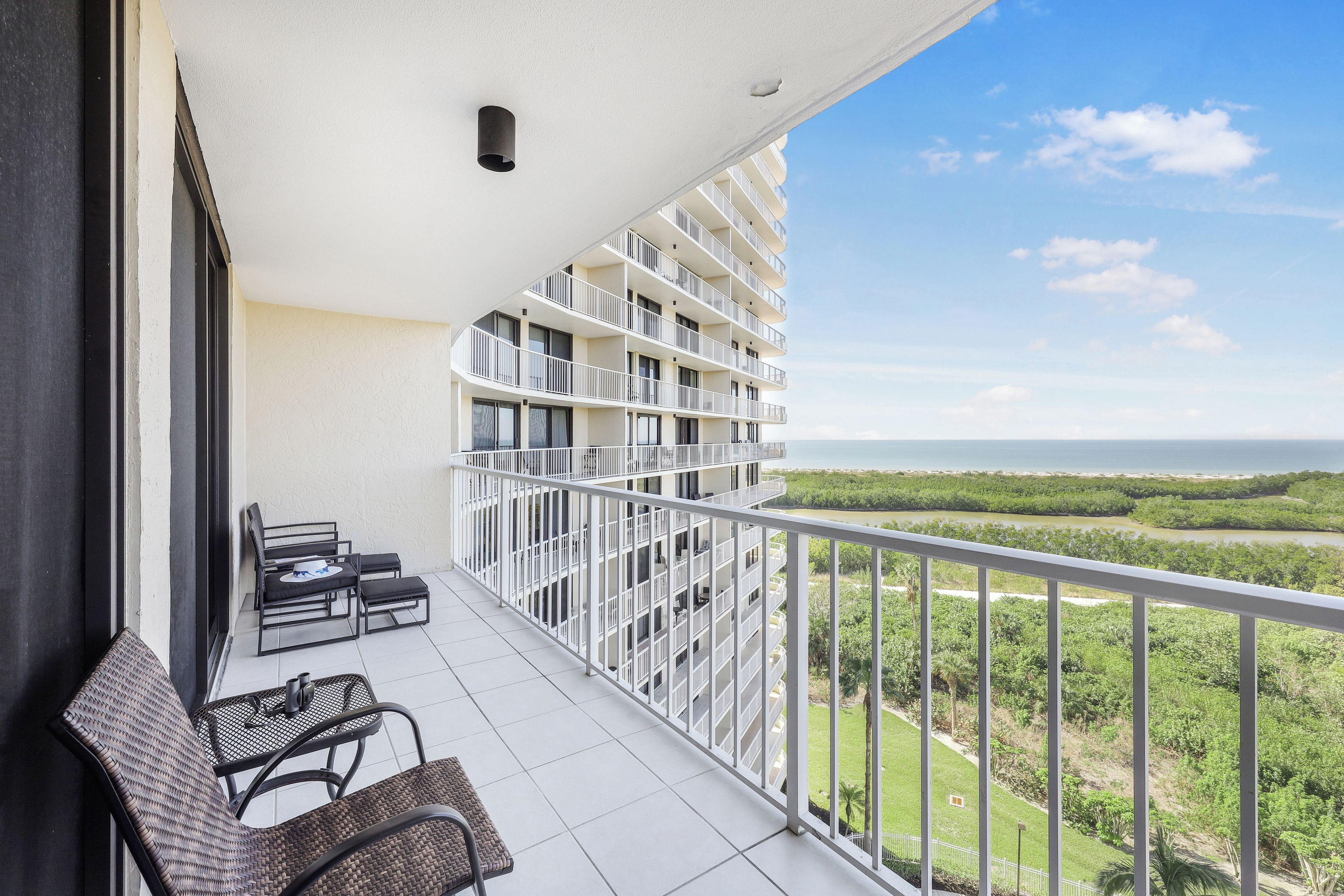 A balcony with a view of a river and greenery, furnished with wicker chairs and a small table.