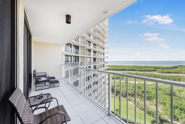 A balcony with a view of a river and greenery, furnished with wicker chairs and a small table.
