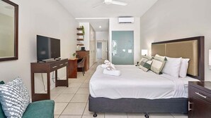 Hotellihuone, jossa on sänky, työpöytä, televisio ja kattotuuletin.