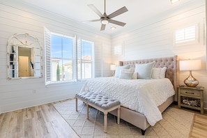 Quarto com uma cama grande, um ventilador de teto e uma janela com persianas.
