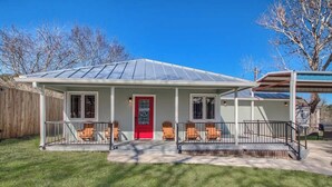 A house with a red door, a covered porch with chairs, and a clear sky. - PRD 2495 Ponderosa Country Haus (New Braunfels)