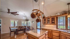 A spacious kitchen with wooden cabinets, a granite countertop, and a dining area with a bench and chairs. - PRD 2495 Ponderosa Country Haus (New Braunfels)