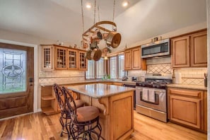 A kitchen with wooden cabinets, a central island, stainless steel appliances, and a hanging pot rack.