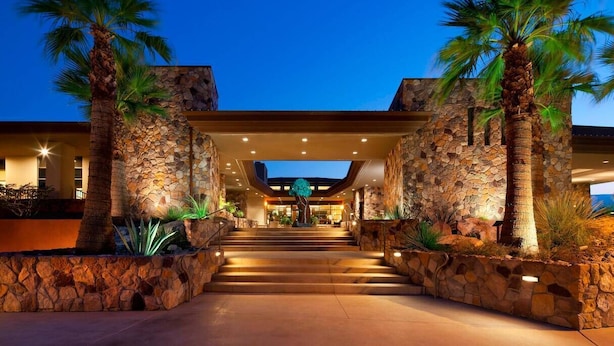 A hotel entrance with a stone facade, palm trees, and a staircase leading to the lobby.