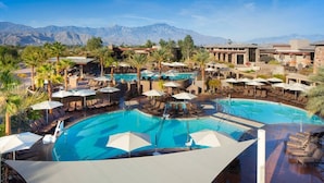 A resort pool area with multiple pools, lounge chairs, umbrellas, and palm trees.