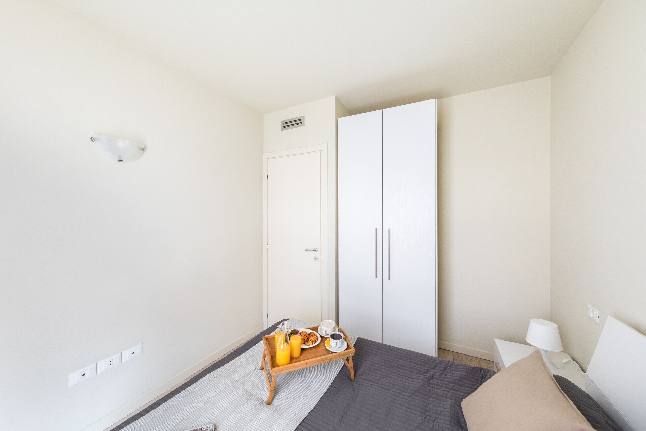 Une chambre à coucher comprenant un lit, une table de chevet, une lampe, une armoire et un plateau avec des articles pour le petit-déjeuner.