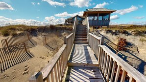 Una pasarela de madera que conduce a una casa de playa con balcón con vista al océano.
