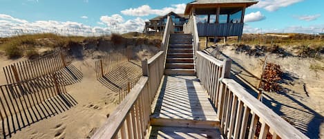 A wooden boardwalk leading to a beach house with a balcony overlooking the ocean.