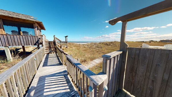 A wooden boardwalk leading to a beach area with a wooden structure on the left.