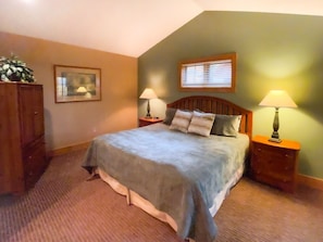 A bedroom with a bed, two bedside tables, a nightstand, a dresser, a window with blinds, and a framed picture on the wall.