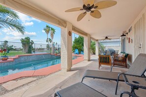A covered outdoor area with a pool, lounge chairs, and a ceiling fan.