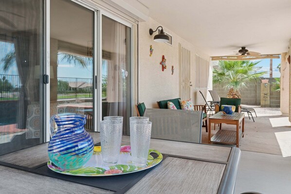 A patio area with a table, chairs, a sofa, and a sliding glass door leading to a view of palm trees. - Painted Mountain Golf Retreat /On Golf Course/Private Heated Pool (Mesa)