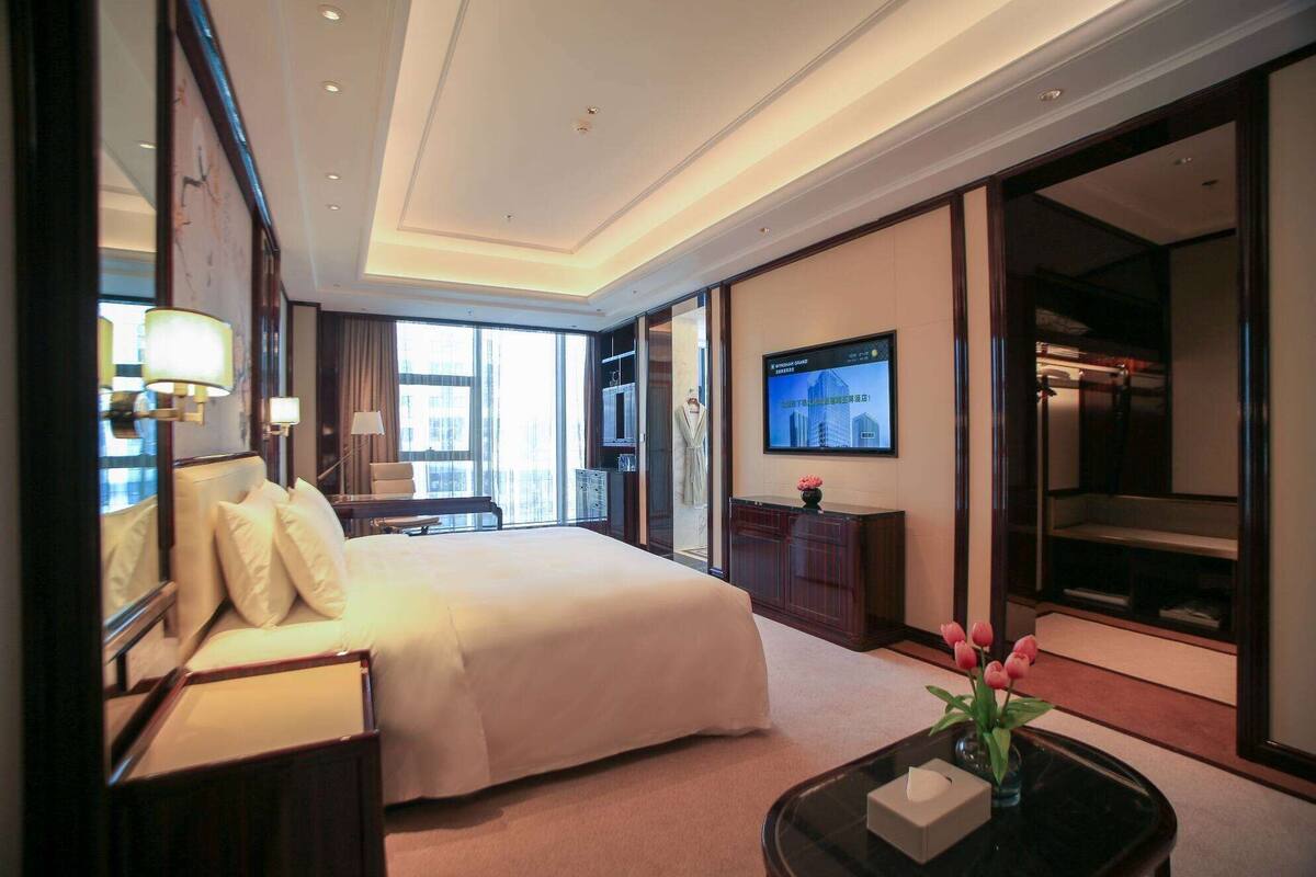 Ein Hotelzimmer mit einem großen Bett, einem Schreibtisch, einem Fernseher und Blick auf die Stadt durch das Fenster.