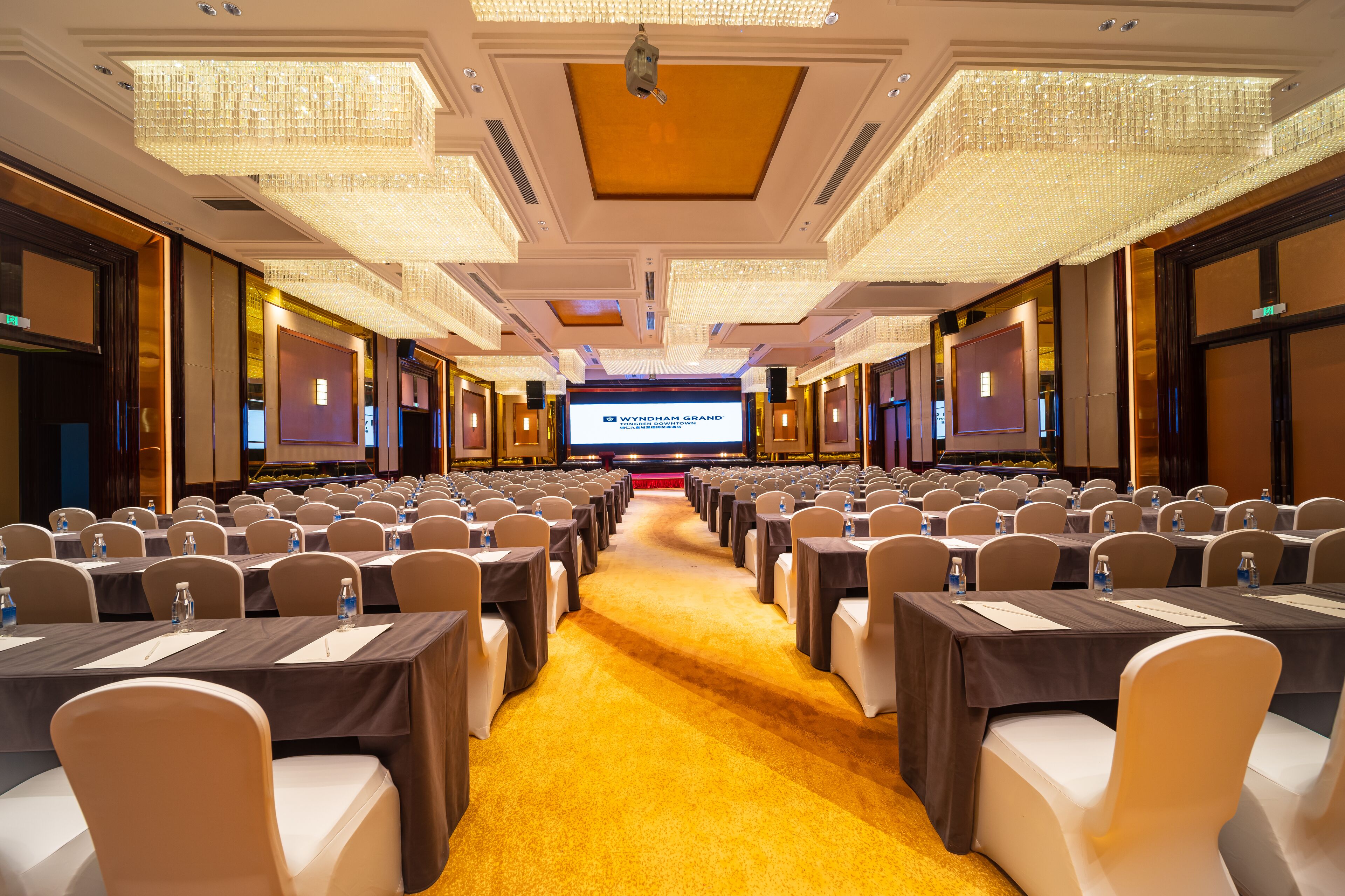 A conference room with rows of tables and chairs, a carpeted floor, and a large screen at the front.