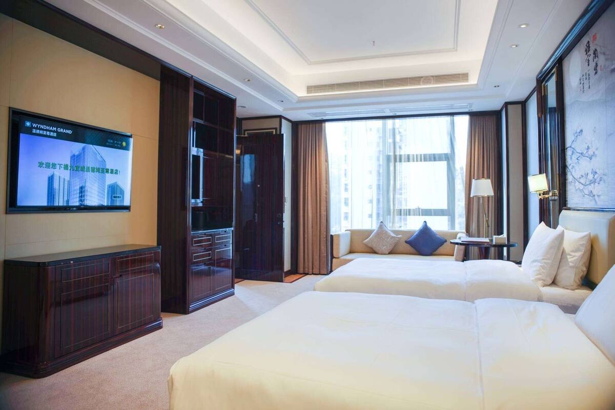 Ein Hotelzimmer mit einem großen Bett, einem an der Wand befestigten Fernseher und Blick auf die Stadt.