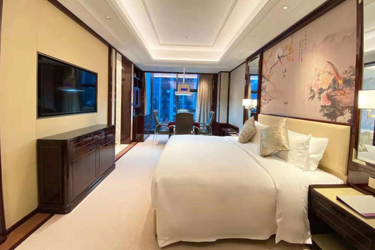 Ein Hotelzimmer mit einem großen Bett, einem Flachbildfernseher, einem Schreibtisch und einem Stuhl.