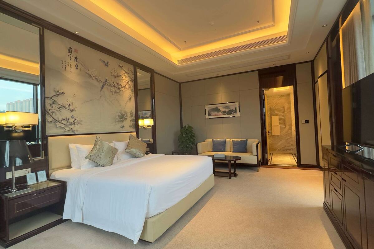 Ein Hotelzimmer mit einem großen Bett, einer Sitzecke, einem Fernseher und einem Schreibtisch mit Lampe.