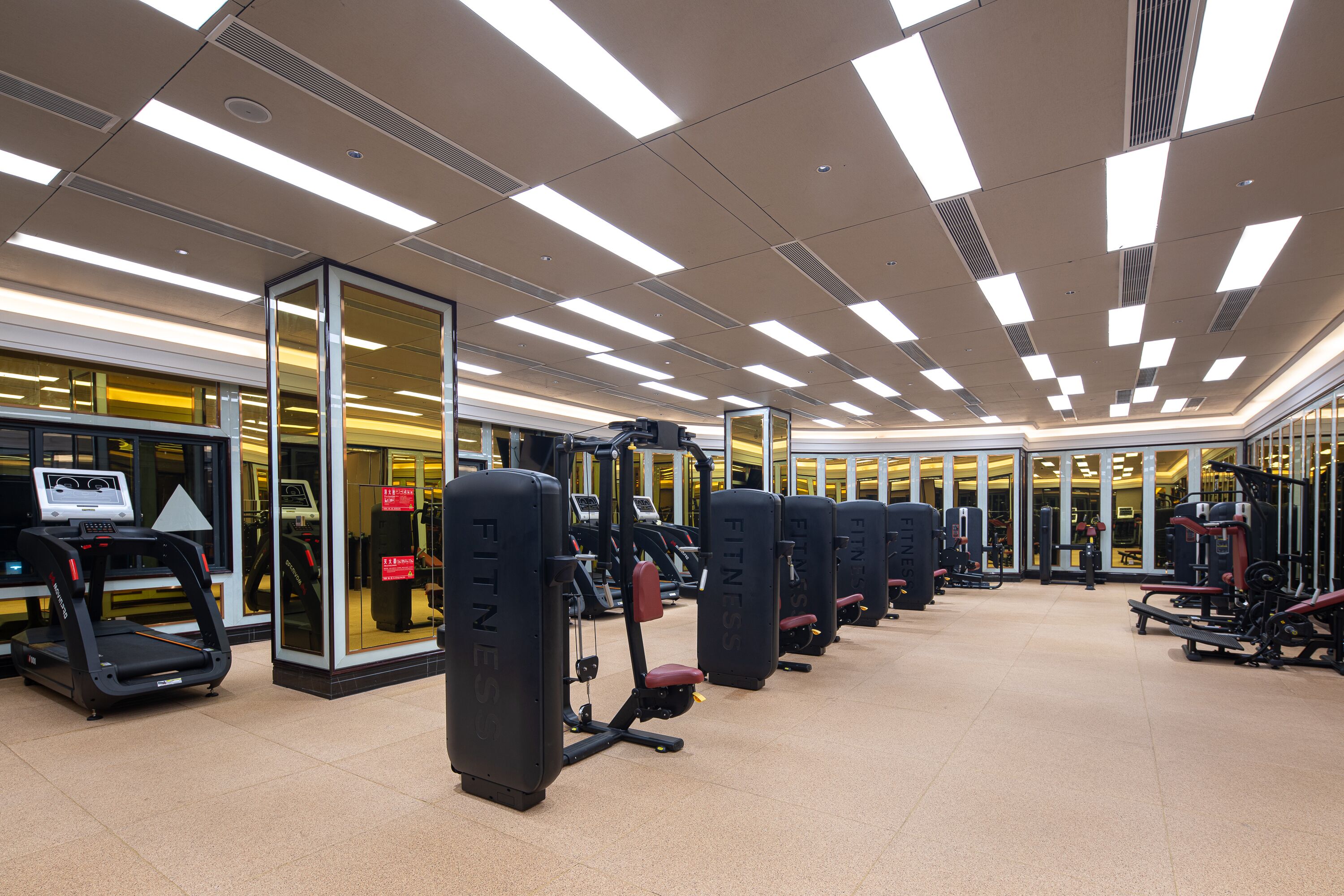 A gym with multiple exercise machines, a treadmill, and a mirrored wall.