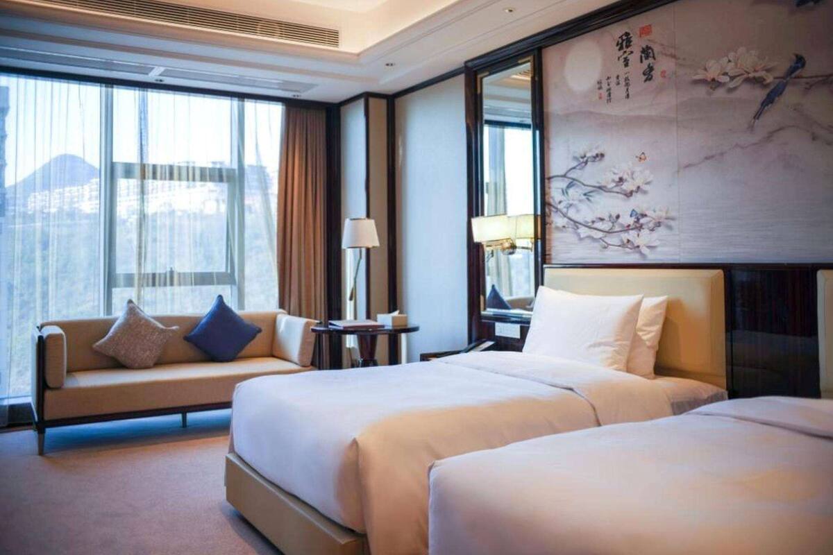 Ein Hotelzimmer mit zwei Betten, einer Schlafcouch, einem Fenster mit Vorhängen und einem Bild an der Wand.