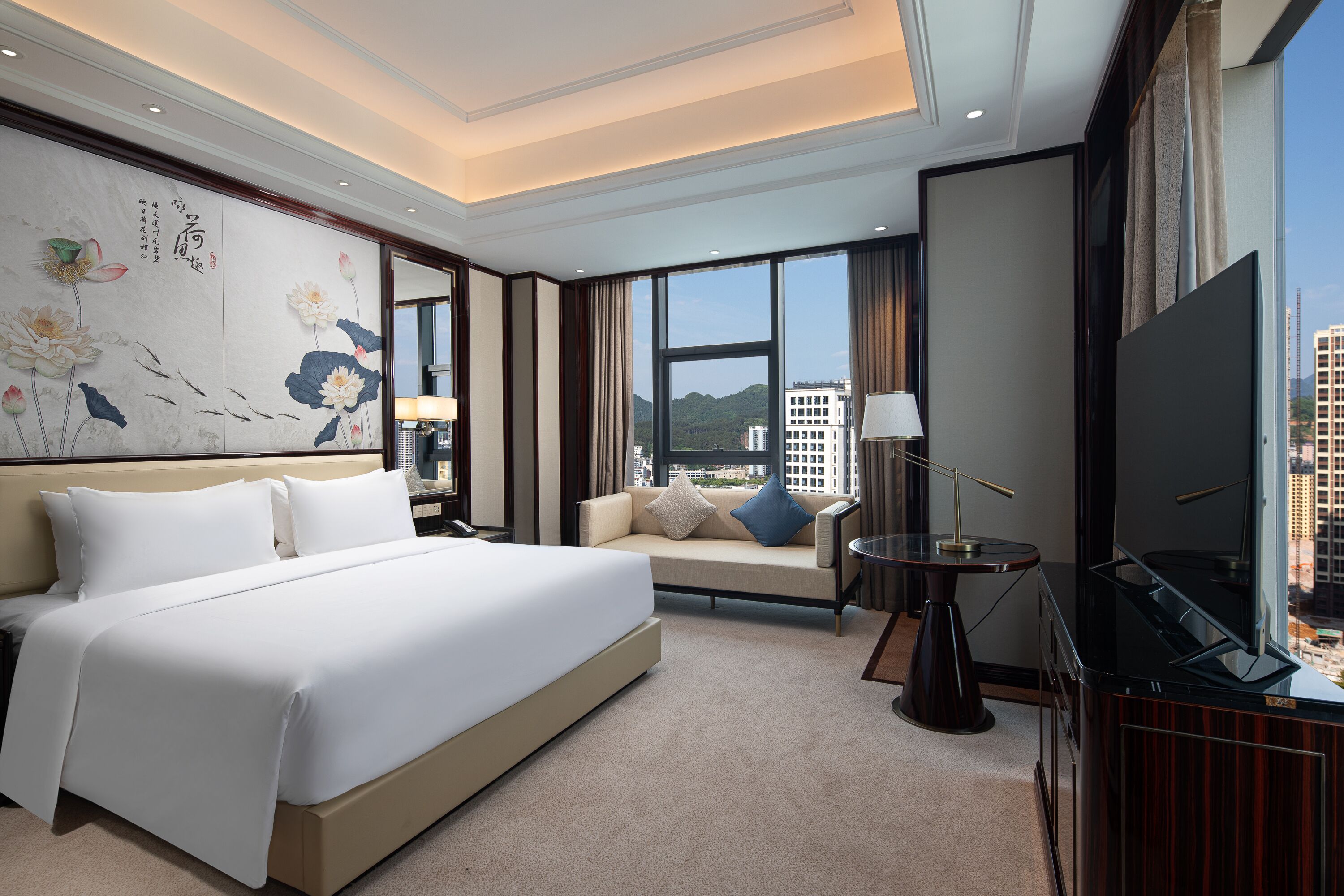 A hotel room with a large bed, a sofa, a TV, and a view of the city.