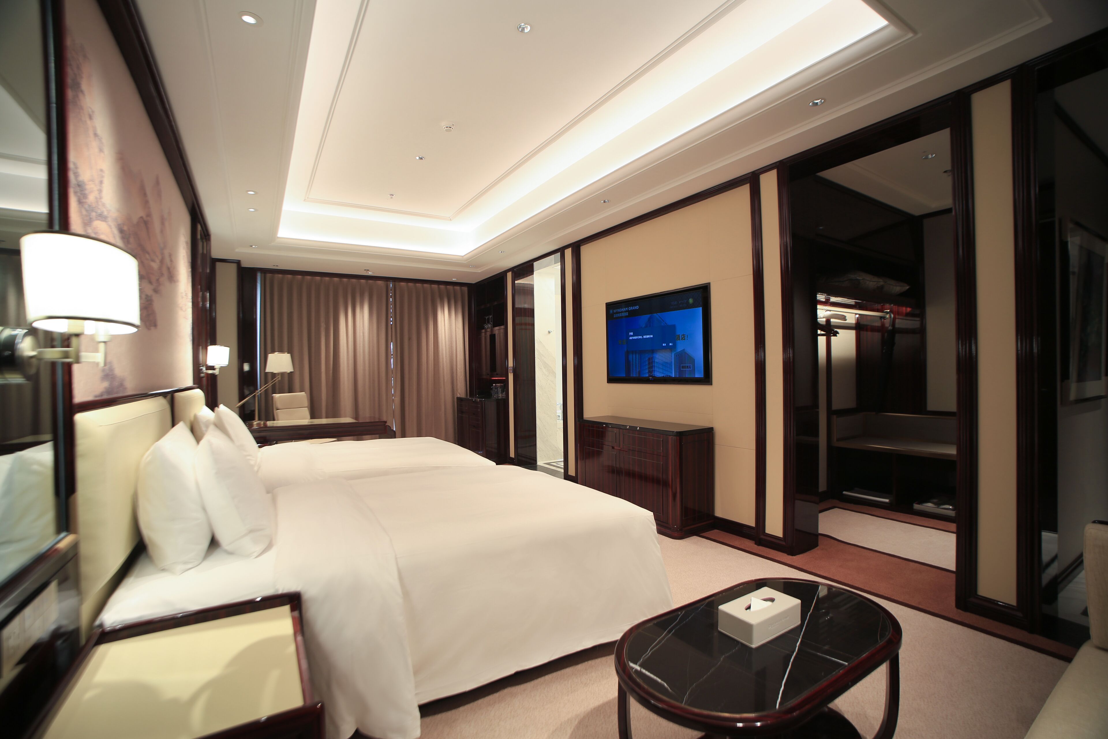 Quarto de hotel com uma cama grande, televisão, escrivaninha e guarda-roupa.