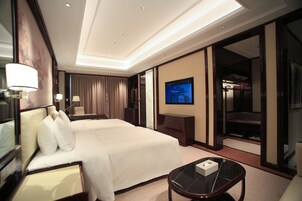 Quarto de hotel com uma cama grande, televisão, escrivaninha e guarda-roupa.