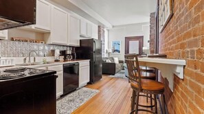 A compact kitchen with white cabinets, a black refrigerator, and a stove. There is a wooden bar stool and a rug on the floor. - Chic 2BR: Near Downtown, Copper Mountain (Leadville)