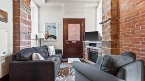 A cozy living room with a fireplace, a television, and a door with a poster. - Chic 2BR: Near Downtown, Copper Mountain (Leadville)