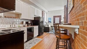 A compact kitchen with white cabinets, a black refrigerator, and a stove. There is a wooden bar stool and a rug on the floor. - Chic 2BR: Near Downtown, Copper Mountain (Leadville)