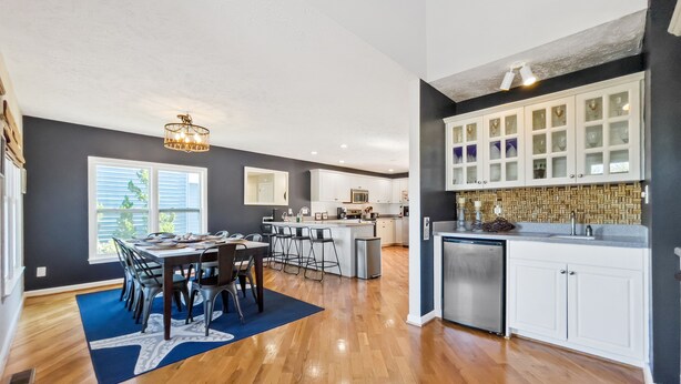 A modern kitchen with white cabinets, a central island, and a dining area with a blue rug. - Spacious 5 BR House with Private Pool and ICW views (Holden Beach)