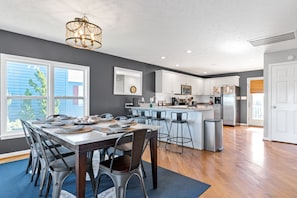 A modern kitchen with a dining area, featuring a large island, stainless steel appliances, and a chandelier.