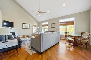 A spacious living room with a grey sofa, wooden dining table, and chairs.