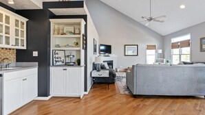 A spacious living area with a grey sofa, a fireplace, and a kitchen with white cabinets. - Spacious 5 BR House with Private Pool and ICW views (Holden Beach)