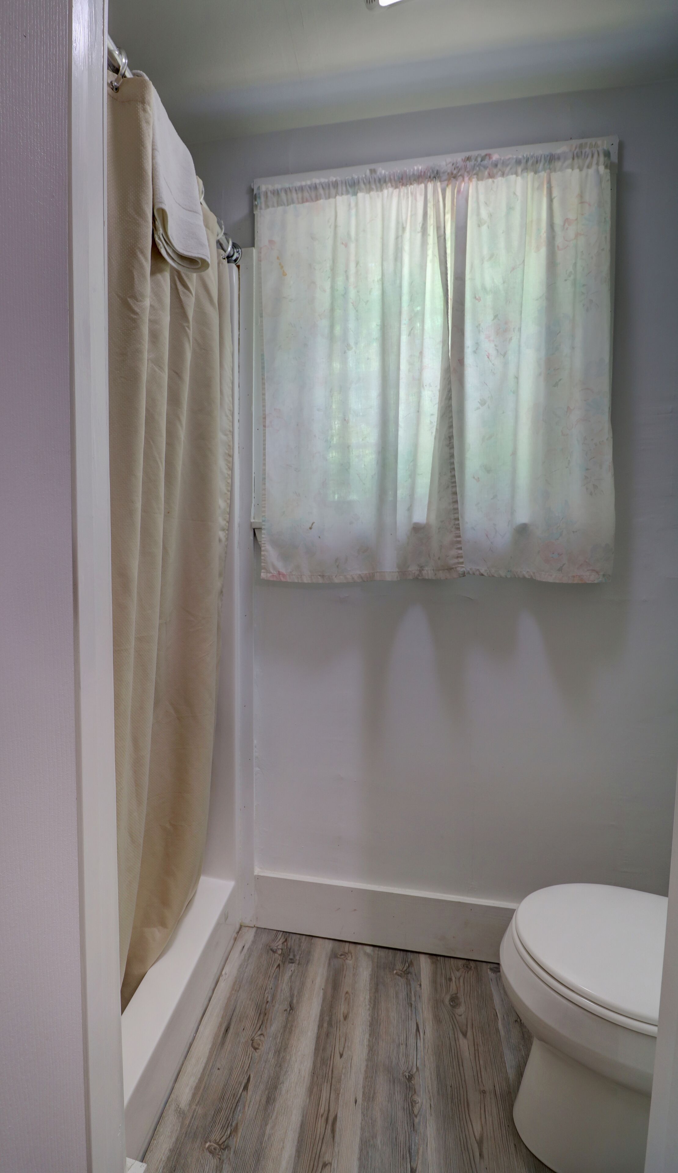 A bathroom with a shower curtain, a toilet, and a window with a floral pattern.