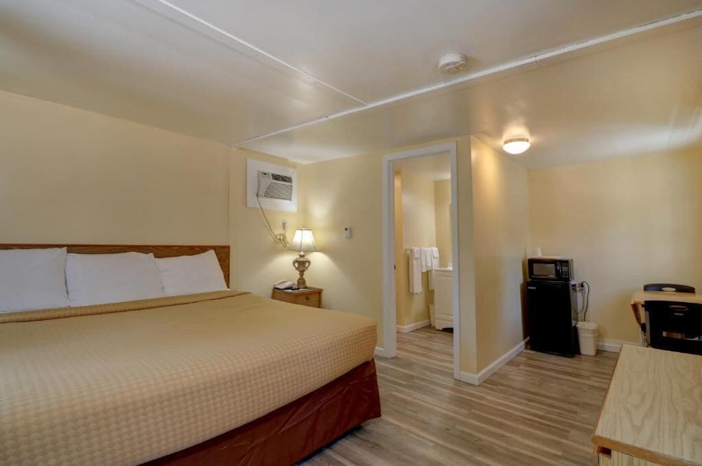 A hotel room with a bed, bedside lamp, a desk, a microwave, and a small kitchenette.