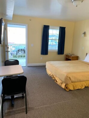 A hotel room with a bed, a desk, a chair, a window with curtains, and a view of the outside.