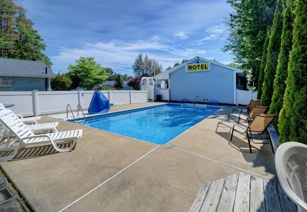 A motel with a swimming pool, lounge chairs, and a covered area.