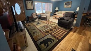 Ein Wohnzimmer mit blauer Wand, Deckenventilator, Kamin und großem Teppich mit Tiermuster.