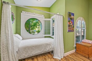 Un dormitorio con cama con dosel, una ventana redonda y vistas al verdor.