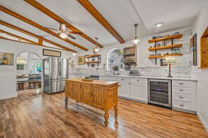 Una cocina con vigas de madera, una isla central, electrodomésticos de acero inoxidable y estantes abiertos.