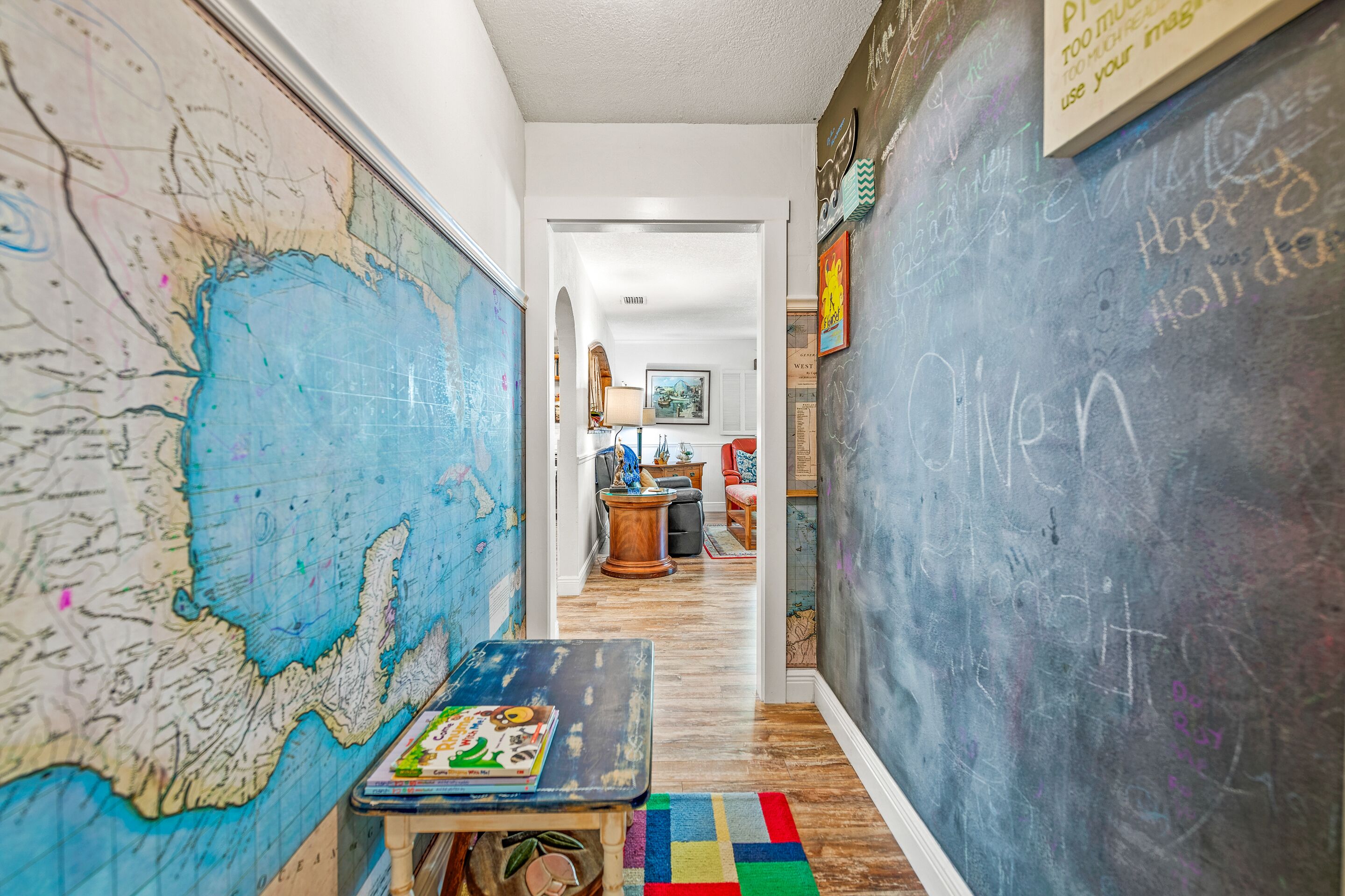 A hallway with a large map on the left, a chalkboard on the right, and a small table with a board game in the center.