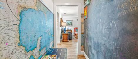 A hallway with a large map on the left, a chalkboard on the right, and a small table with a board game in the center.
