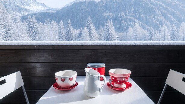 A table with a white pitcher, two red cups with heart designs, and a red container with a lid, set against a snowy mountain backdrop. - Bel Apt Near The Slopes Argentiere (Chamonix-Mont-Blanc)