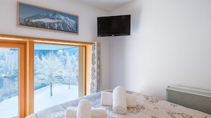 A bedroom with a large window, a bed with a floral bedspread, and a flat-screen TV mounted on the wall. - Bel Apt Near The Slopes Argentiere (Chamonix-Mont-Blanc)